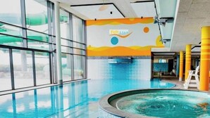 Ein beheiztes Hallenbad mit großen Glaswänden, einer Whirl-Badewanne und farbenfroher Wandgestaltung.