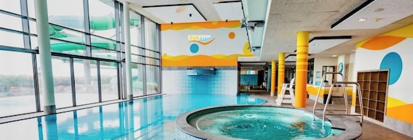 Ein beheiztes Hallenbad mit großen Glaswänden, einer Whirl-Badewanne und farbenfroher Wandgestaltung.