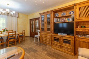 Un soggiorno con rivestimento in legno, zona pranzo, televisione ed elementi a scaffale.