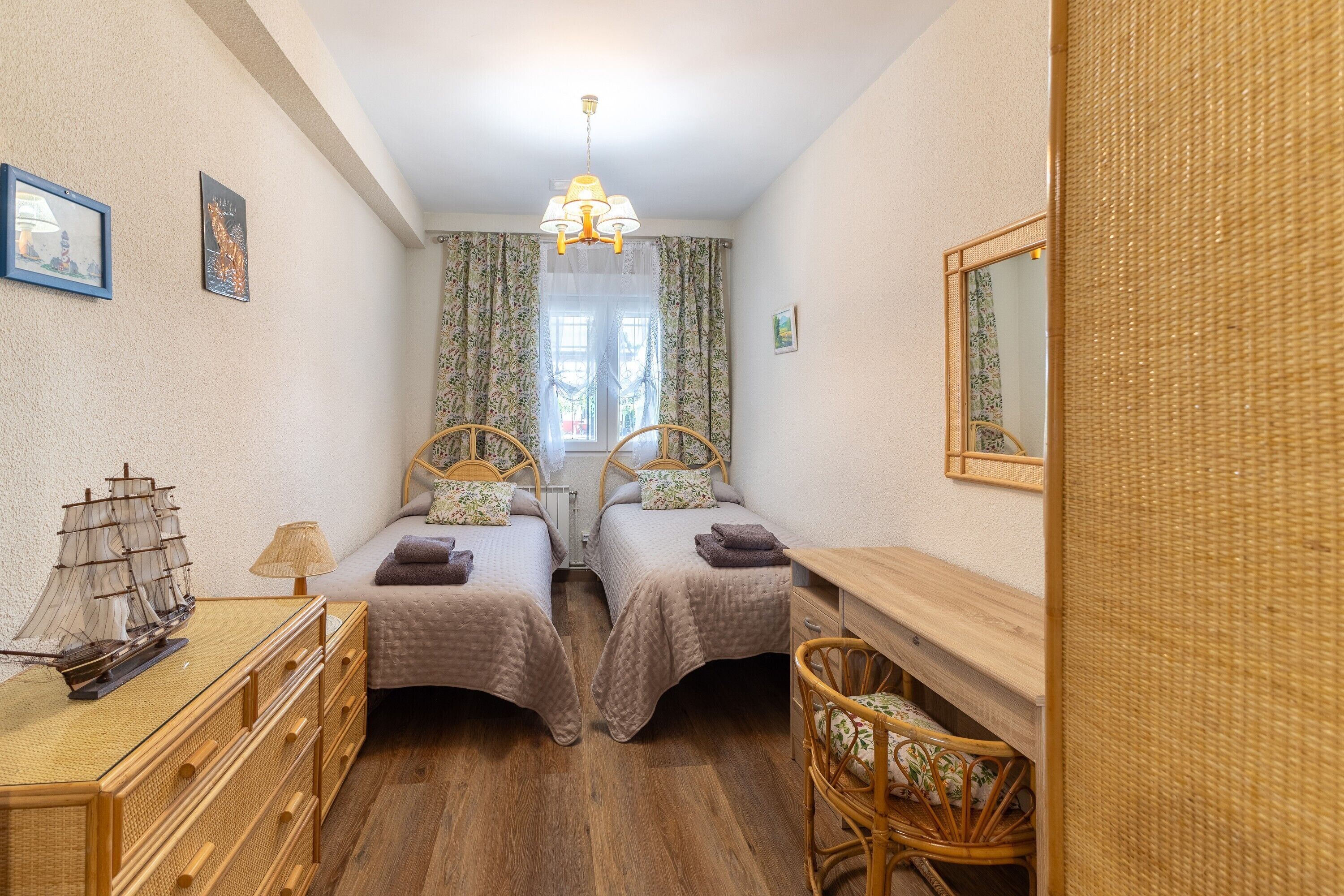 Ein Schlafzimmer mit zwei Betten, einem Holzkleiderschrank, einem Stuhl, einem Schreibtisch, einem Spiegel und einem Schiffsmodell.