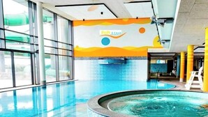Una piscina interna con pareti in vetro trasparente, una vasca idromassaggio e un murale colorato.