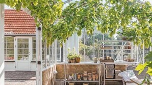 Un invernadero con estructura de vidrio, plantas en macetas y una silla de mimbre.