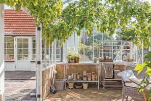 Een kas met een glazen structuur, potplanten en een rieten stoel.