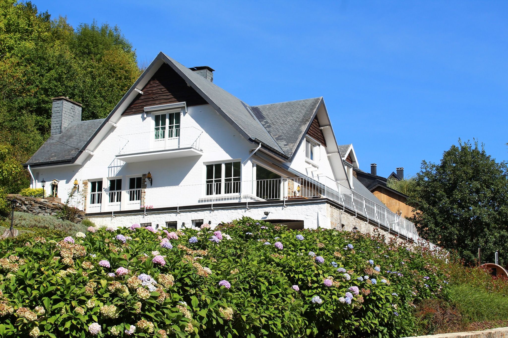 A two-story house with a white exterior, a balcony, and a garden with hydrangeas.