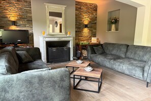 A living room with a fireplace, stone wall, grey sofas, and a flat-screen TV.