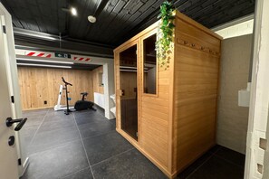 A wooden sauna with a glass door, a treadmill, and a weight bench in a room with tiled flooring and a dark ceiling.
