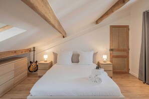 Ein Schlafzimmer mit einem großen Bett, Holzbalken, einer Gitarre und einem Dachfenster.