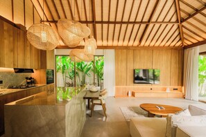 A modern interior with a kitchen, dining area, and living space, featuring wooden beams, a TV, and a large window with greenery. - Apura Villa by Betterplace (Ubud)