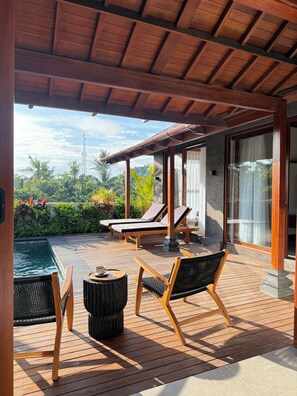 A wooden deck with lounge chairs, a small table, and a pool. - Apura Villa by Betterplace (Ubud)