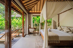 A bedroom with a canopy bed, a desk, and a chair, with a view of lush greenery outside. - Apura Villa by Betterplace (Ubud)