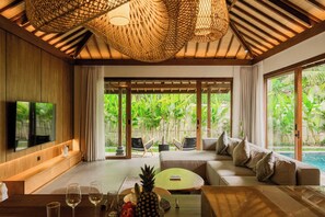 A modern living room with a TV, sofa, coffee table, and a view of a pool and greenery. - Apura Villa by Betterplace (Ubud)