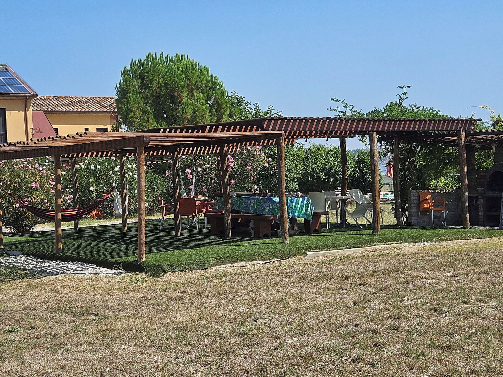 Een overdekt buitengebied met tafels, stoelen, een hangmat en een pergola.