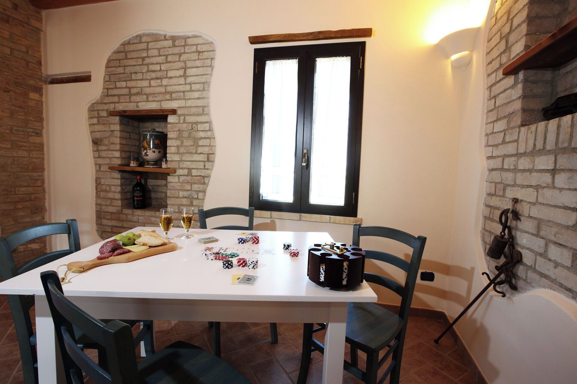 A dining area with a brick fireplace, a window, and a table set with food and playing cards.