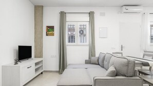 Ein modernes Wohnzimmer mit einer Couch, einem Fernseher und einem Fenster mit Vorhängen.