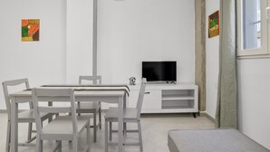 Ein modernes Wohnzimmer mit Esstisch, Stühlen, einem Flachbildfernseher und Kunstwerken an den Wänden.
