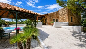 Ein überdachter Außenbereich mit Pool, Steinhaus und Grünflächen.