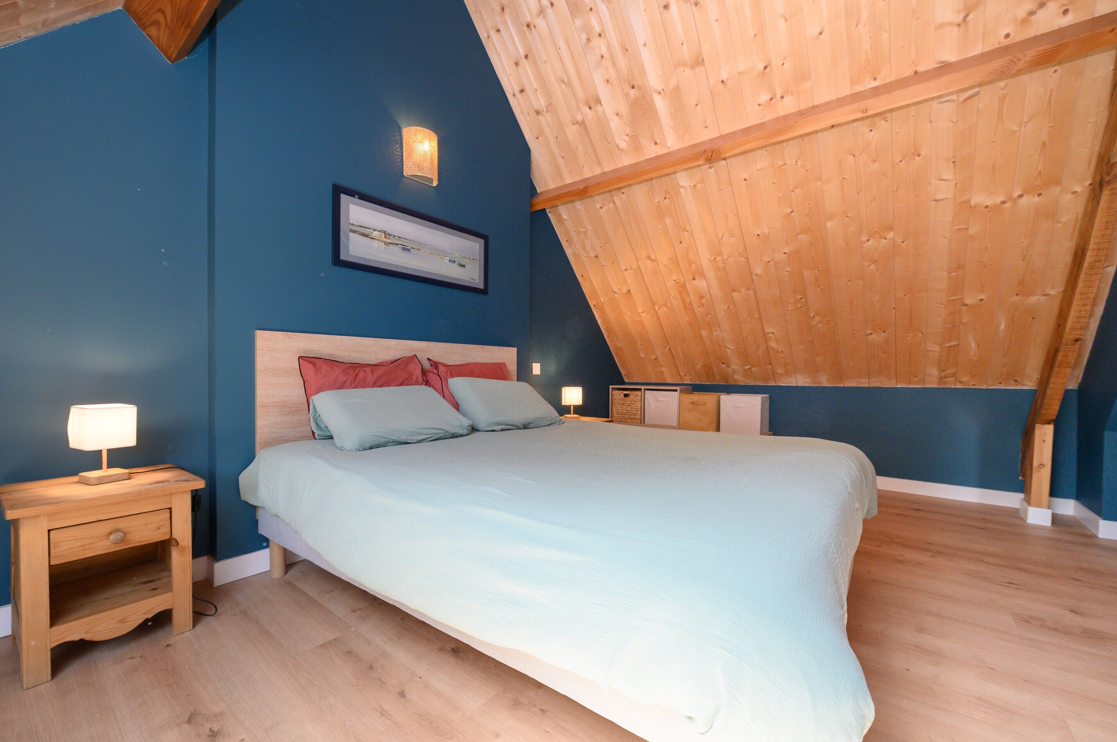 A bedroom with a bed, nightstands, a wall-mounted lamp, and a framed picture.