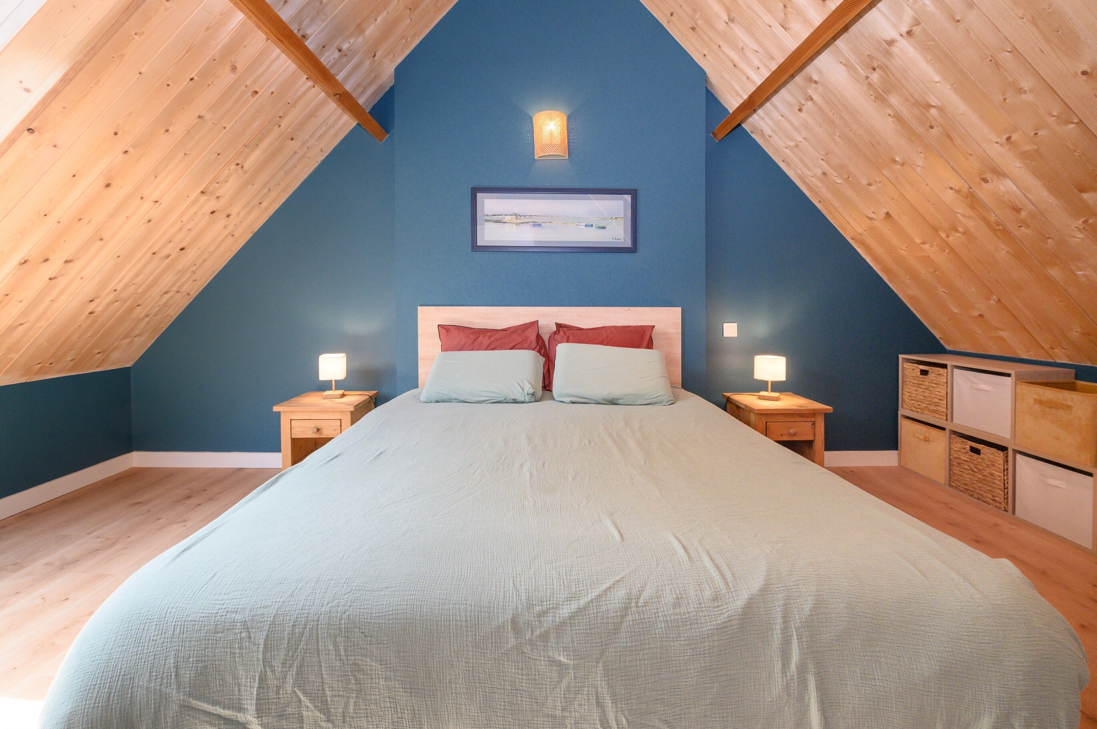 A bedroom with a sloped ceiling, a bed with pillows, bedside lamps, and a framed picture on the wall.