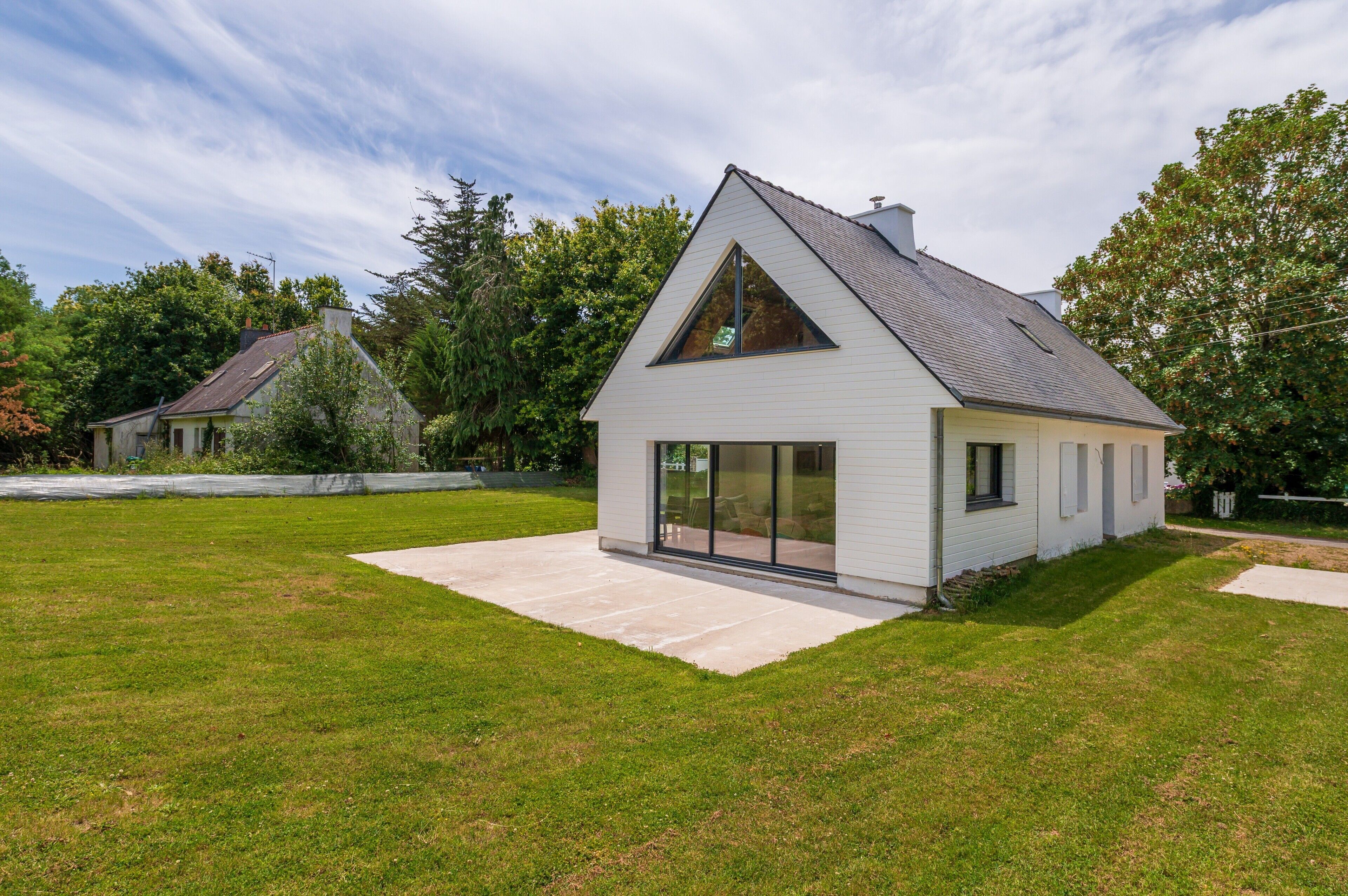 A modern house with a large glass door, a sloped roof, and a well-maintained lawn.