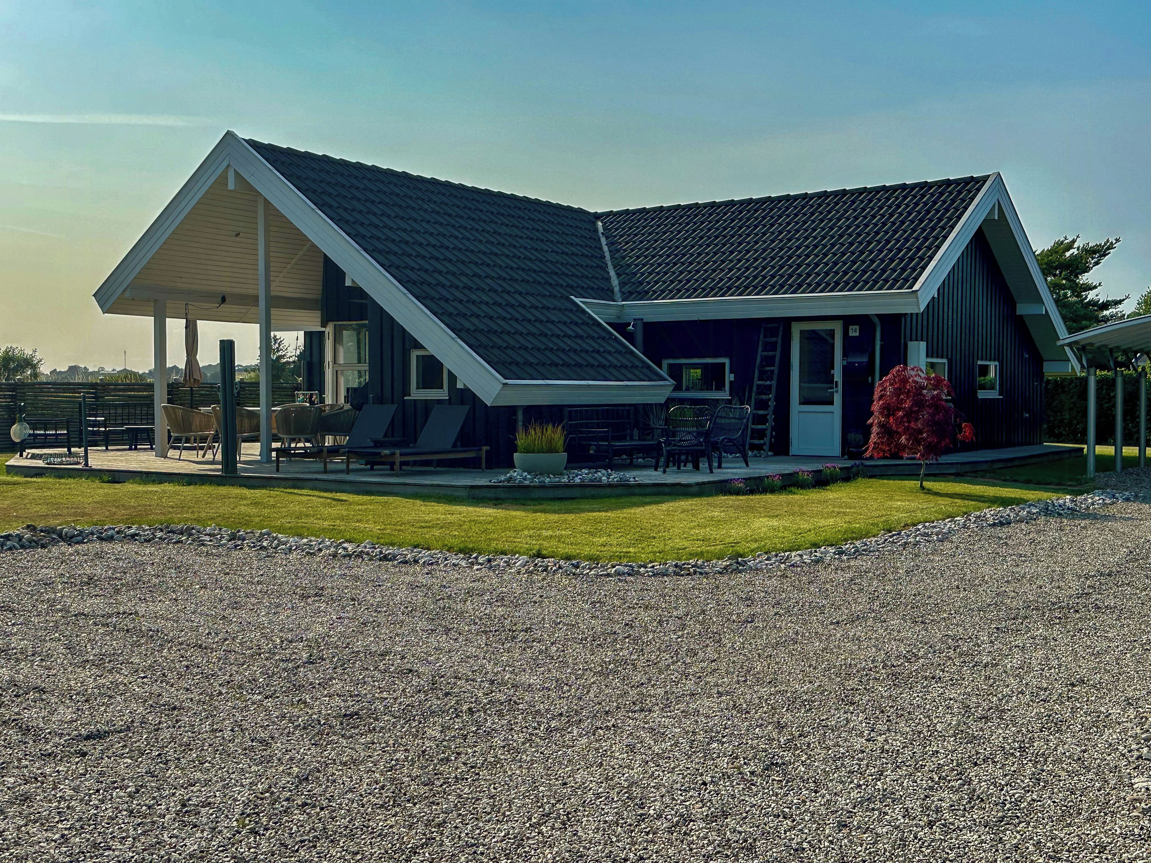 A modern house with a covered patio, a gravel driveway, and a well-maintained lawn.