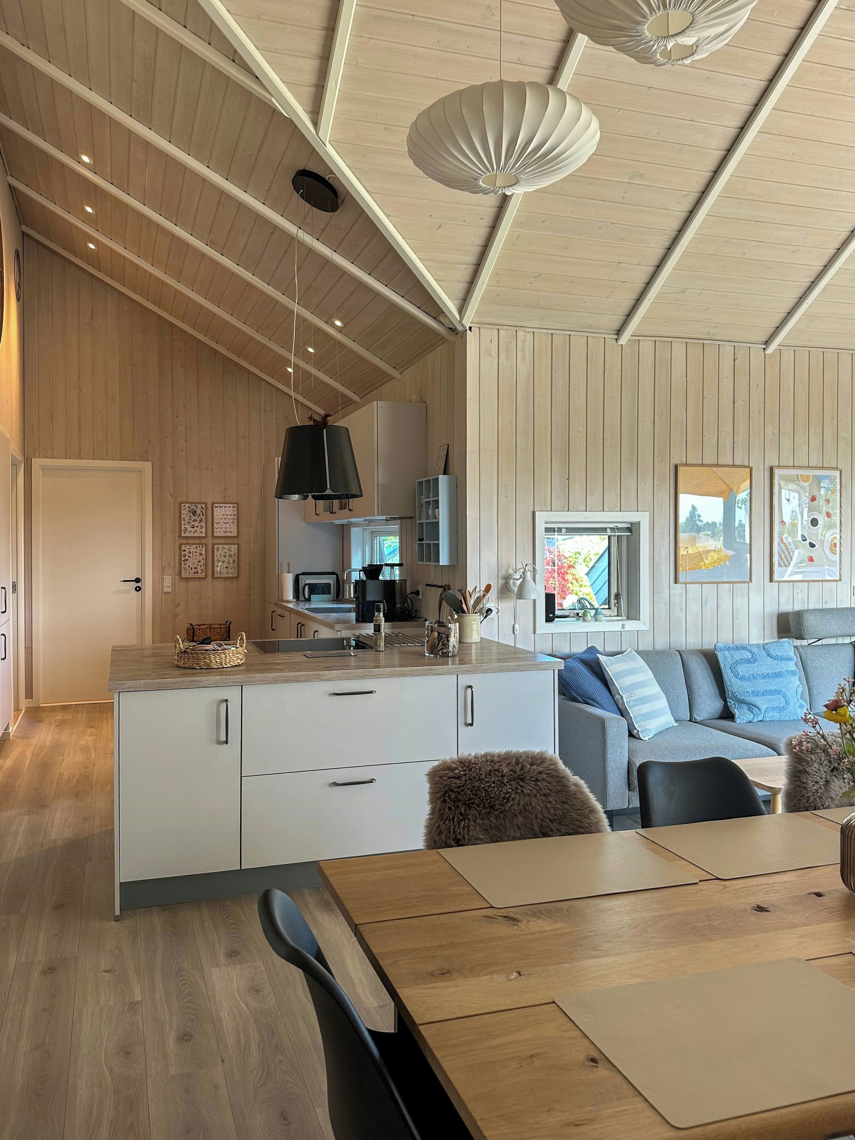 Una cocina moderna con armarios de madera, un comedor con mesa de madera y un sofá gris con cojines decorativos.