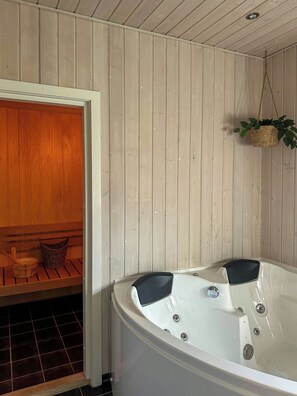 Ein Spa-Raum mit einer hölzernen Sitzbank, einer weißen Badewanne und einer hängenden Pflanze.