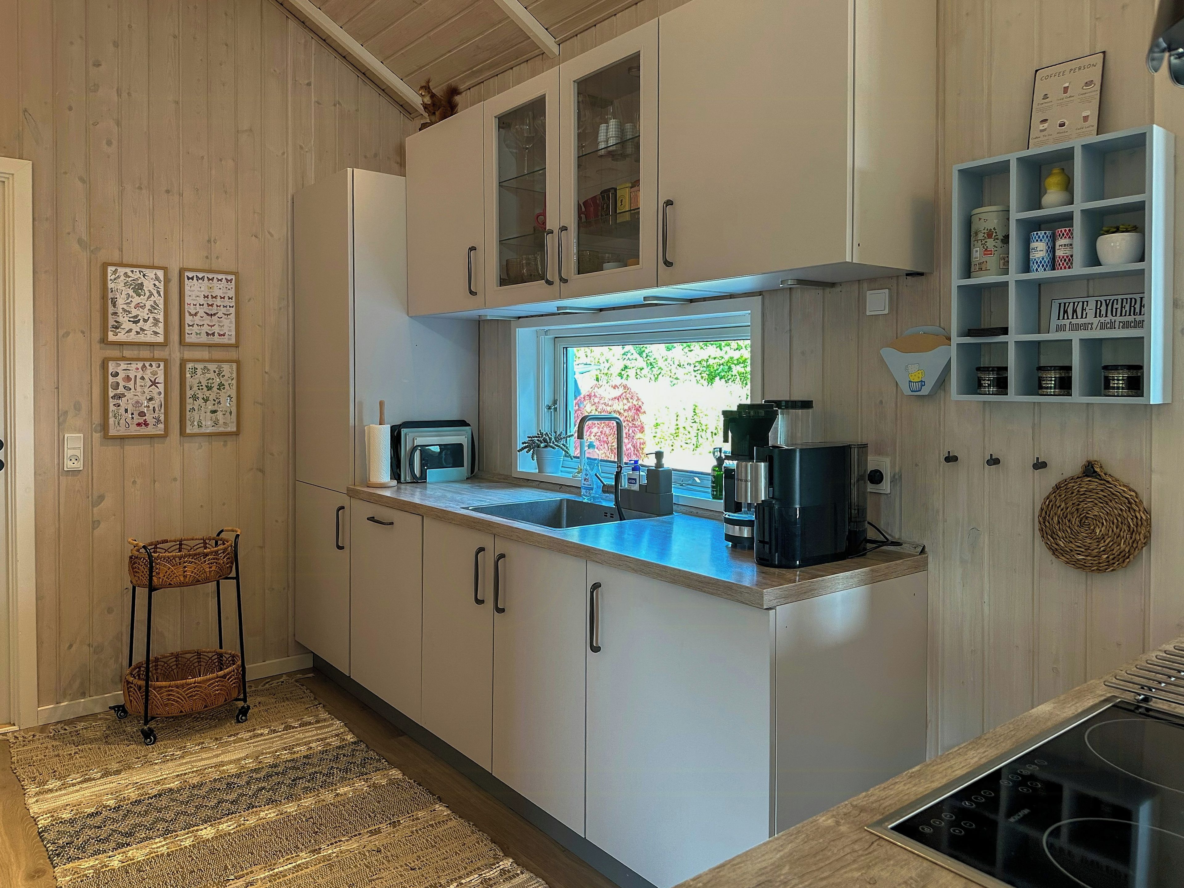 A kitchen with a built-in stove, a coffee machine, and a window with a view of greenery.