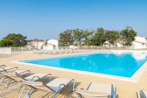 Une piscine rectangulaire à l’eau d’un bleu limpide, entourée de chaises longues et d’une clôture.