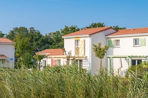 Une rangée de bâtiments blancs aux toits recouverts de tuiles rouges, aux volets verts, sous un ciel d’un bleu limpide.