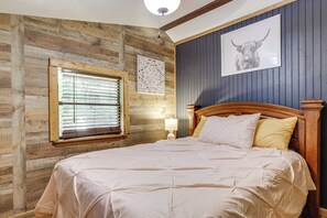 Ein Schlafzimmer mit Holzwand, einem großen Bett mit Kopfteil, einem Fenster mit Jalousien und einem an der Wand befestigten Bild.