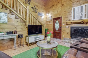 Ein Holzinterieur mit Treppe, Flachbildfernseher, Ledersofa und Kamin.