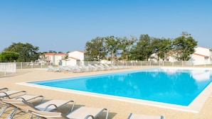 Une piscine rectangulaire à l’eau d’un bleu limpide, entourée de chaises longues et d’une clôture.
