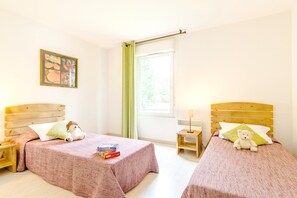 A room with two beds, a nightstand, a window with curtains, and a wall-mounted picture.