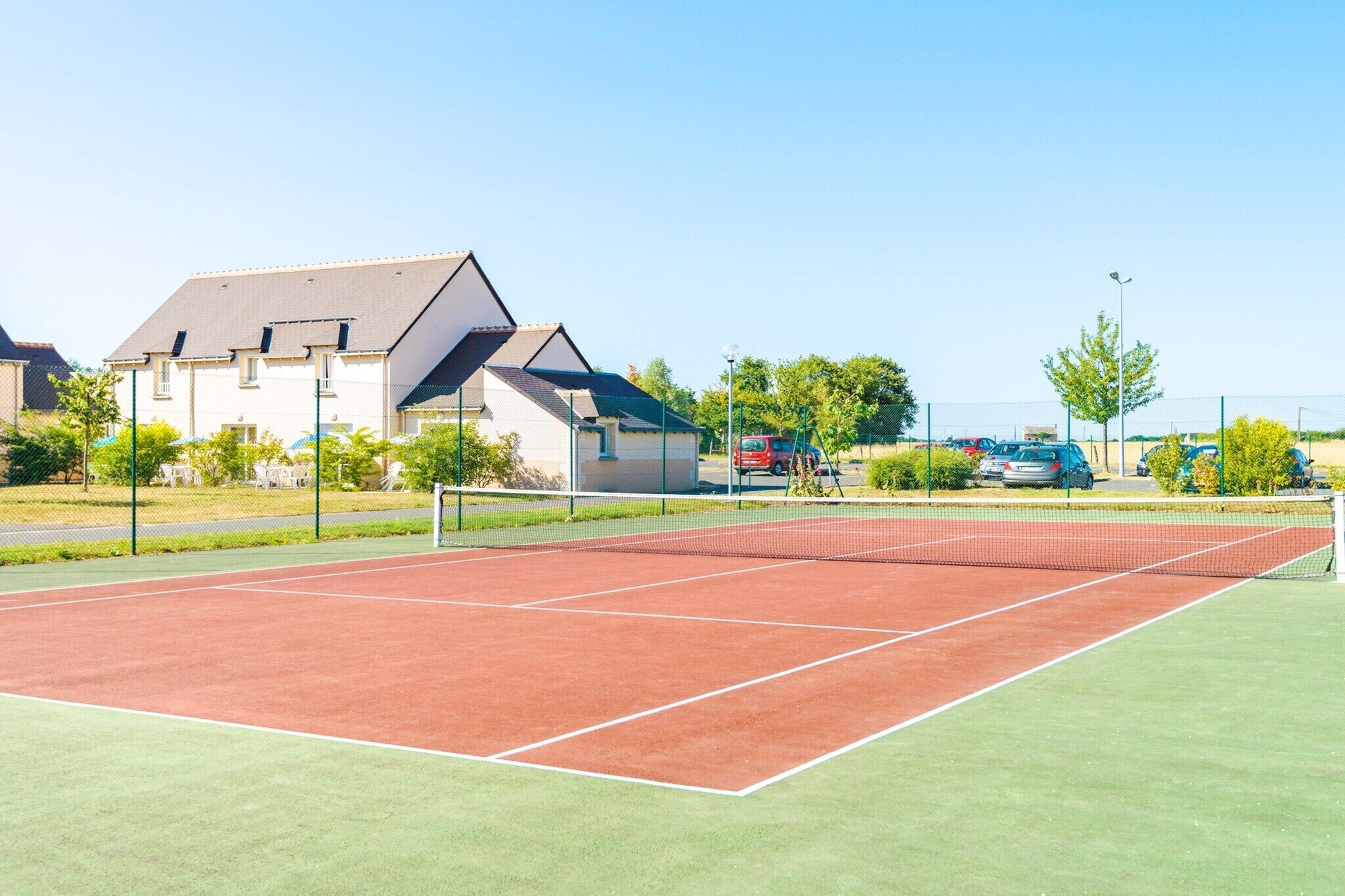 A tennis court with a net, surrounded by a fence, and houses in the background.