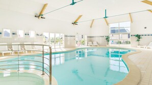 Ein Hallenbad mit klarem Wasser, weißen Liegestühlen und großen Fenstern.