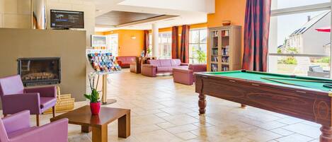 A billiards table, sofas, a fireplace, and a television in a well-lit room with large windows.