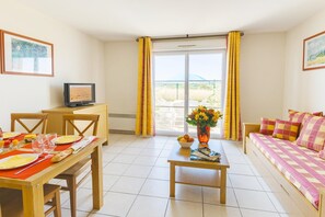 A room with a dining table set for two, a sofa, a TV, and a window with curtains. - Loire Valley Duplex Maisonette (Azay-le-Rideau)