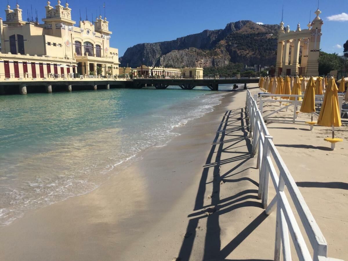 A beach with a promenade, a bridge, and buildings with classical architecture.