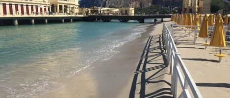 A beach with a promenade, a bridge, and buildings with classical architecture.