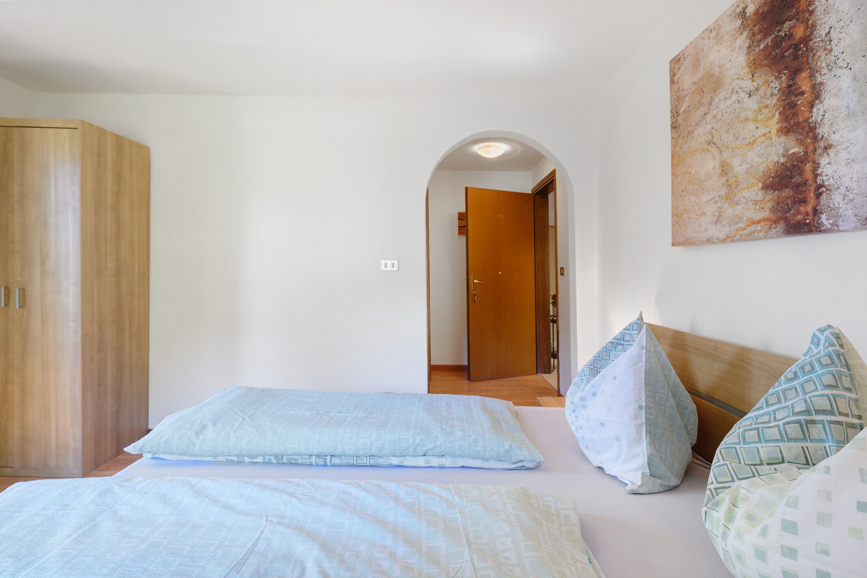 Un dormitorio con cama, almohadas, un armario y una puerta que da a otra habitación.