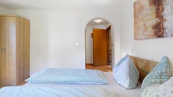 Un dormitorio con cama, almohadas, un armario y una puerta que da a otra habitación.
