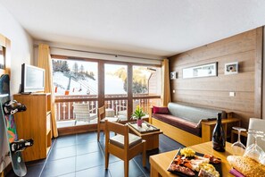 A cozy room with a sofa, a dining table with food, a TV, and a ski lift view. - Alpine Duplex Sanctuary for Groups (Saint-Lary-Soulan)