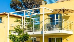 A yellow building with a balcony, glass railings, and a tree in the background. - Seaside Apartment for 4 in Var (Six-Fours-les-Plages)