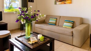 A living room with a beige sofa, a glass vase with flowers, a coffee table, and a window with a view of greenery. - Seaside Apartment for 4 in Var (Six-Fours-les-Plages)