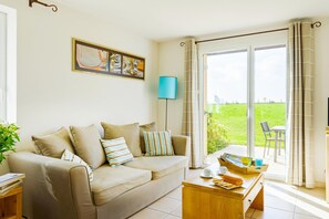 A living room with a sofa, a coffee table, a lamp, and a view of a green landscape through a glass door. - Coastal Apartment Escape in Cancale (Cancale)
