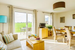 A living room with a sofa, coffee table, TV, and dining area with chairs and a table. - Coastal Apartment Escape in Cancale (Cancale)