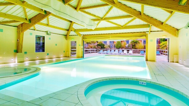 En inomhuspool med ett kaklat golv, en träkonstruktion i taket och fri utsikt mot omgivningen.