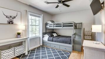 Una habitación con una cama litera, un escritorio con lámpara, un ventilador de techo y una ventana con cortinas.