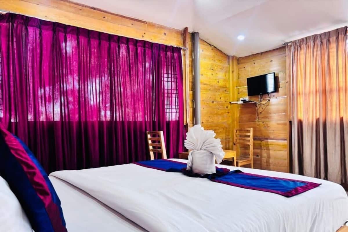 A hotel room with a bed, curtains, a television, and a wooden wall.
