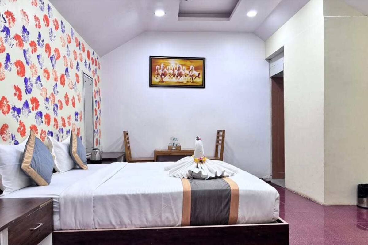 A hotel room with a bed, a nightstand, a desk, a chair, a painting on the wall, and a door.